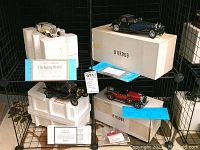 Four model cars displayed with original foam packaging and certificates of authenticity visible for the Jaguar SS-100 and Ford Model T.