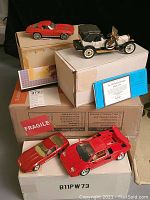 Four model cars shown on and beside original boxes. Included are a white 1912 Packard Victoria, red 1963 Chevrolet Corvette Sting Ray, red 1988 Lamborghini Countach, and red 1987 Chevrolet Corvette with gold roof.