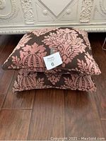 Two stacked square accent cushions with brown fabric and pink floral damask design.
