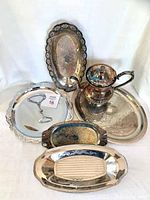 Photo showing one ornate silver plated teapot and five silver plated trays of varying shapes and sizes arranged together, displaying tarnish and need for polishing.