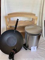 Electric frypan, wooden wine rack, and stainless steel garbage can together with white cloth background.