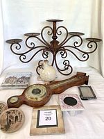 Wide view of lot showing large metal candelabra, wooden barometer, frames, coasters, figurine, and book.