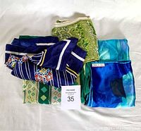 Five vintage neck scarves folded and placed on white surface showing various colors and patterns including blue with stripes and floral, green paisley, and blue tie-dye.