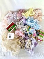 Lot of assorted lace trims in pastel colors including pink, blue, yellow, lavender, and cream with original packaging visible.