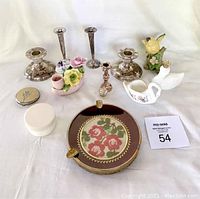 Full lot of silver plated candle holders, floral ceramic figurines, ceramic bird figurine, swan-shaped containers, round embroidered tray, and compact case.