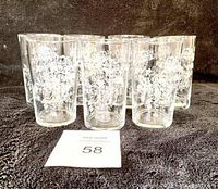Front view of seven clear glasses with white floral patterns on a dark surface.