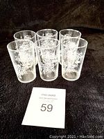 Photo of the set of 6 small clear juice glasses with white floral decoration, arranged with auction tag.