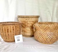 Front view of three wicker buckets placed side by side on white fabric background, showing shapes and weaving patterns.