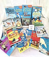 Top-down view of 18 children's books arranged on a white cloth surface. Titles include The Flying Beaver Brothers, Llama Drama, Encyclopedia Brown series, Calamity Sue, Penguin Problems, and others. Bright and colorful illustrated covers featuring animals and human characters.