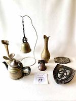 Photo showing all items in the lot including the Wearbrite mini teapot, hanging brass bell, brass vase, cast iron trivet, flower-shaped candle holder, log holder with logs, and embossed metal dish.