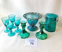 Front view showing all items including four turquoise glasses, two green candlesticks, blue carnival glass pedestal bowl and Avon jar