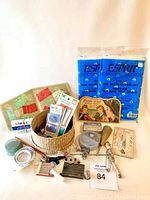 Full display of vintage sewing accessories including basket, fabric packs, pins, needles, tools, and kits arranged on flat surface