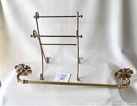 Full view of brass cloth rack with two horizontal bars and towel bar with floral ends, set on white background