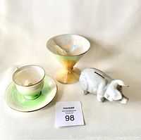 Frontal view of Grimwades teacup, matching green saucer with micro chip, yellow-green lustre ice cream dish, and white piggy bank with coin slot.