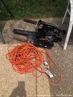 Photo of the lot showing the electric chain saw, hedge trimmer, leaf blower, and orange extension cord on concrete surface outdoors.