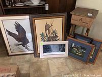 Six various sized art prints leaning against a bookcase and small table, unframed, showing different nature and cottage theme artworks.