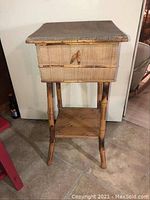 Front view of vintage sewing box on stand showing hinged lid and latch with natural wood finish and worn condition