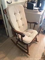 Front angle view of rocking chair with cream tufted cushions tied to wooden frame.