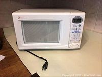 Full view of Daewoo microwave showing white exterior, front door with window, and power cord extending from the back.