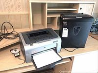 HP LaserJet P1006 printer with paper output tray and Fellowes H-7C shredder placed on wooden desk