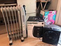 Photo showing the Sunbeam heater with visible control dials, Chefman air fryer in box, and Holmes fan on floor.