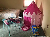 Collapsible pink princess-style playhouse tent alongside Frozen themed children's table and chair with a blue and yellow Dory ride-on toy on carpeted floor.