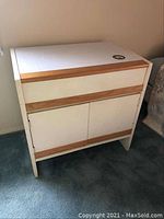 Front view of the white and wood Henry Link cabinet showing drawer, doors, top sticker, and surface condition.