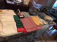 Wide view of table showing assorted table linens, glass serving trays, ceramic plates, bowls, serving dishes, and decorative items.