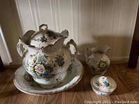 Front view of all four items: large wash basin, urn with lid, small pitcher, and covered dish with lid showing chip