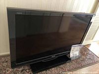 Front view of Sharp Aquos 46-inch flat screen television on a stand showing its black frame and screen size.