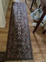 Full view of a rectangular runner rug with floral pattern and bound edges on a hardwood floor.