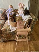 Photo showing full lot arranged on patterned couch including three porcelain dolls, two Boyds Bears plush bears, a wicker basket, wooden doll highchair, and quilted blanket.