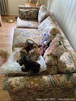 Side/top view of floral upholstered sofa with dolls and stuffed animals on cushions, patterned upholstery with floral and leaf design