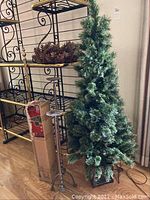 Tall artificial Christmas tree on box base with two metal candle holders and boxed smaller tree next to metal shelving unit