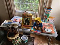 Overview of children's books, Paddington Bear plush, Tinkertoy set and tins on table