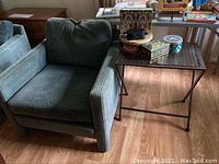 Front angled view of the green corduroy upholstered chair and side table with items on top