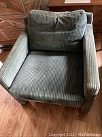 Front view of upholstered armchair showing greenish-blue corduroy fabric and loose back cushion.