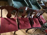 Photo of four wooden chairs, two captain's chairs with armrests and two side chairs with red cushions.