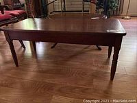 View of entire cherry wood rectangular coffee table from side angle showing turned legs and table top with some scratches