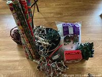 Full view of Christmas lot showing rolls of wrapping paper, string lights in white and green wires, synthetic snow blanket package, and other decoration components.