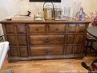 Full view of the wooden buffet, showing top surface with various decor items and front view of drawers and cabinets.