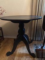 Full view of the round wooden occasional table showing the tabletop and pedestal base with three curved legs.