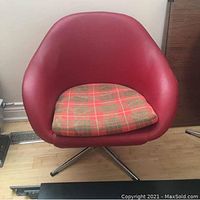 Front view of a vintage MCM swivel bucket chair with red vinyl upholstery and a removable plaid fabric cushion on a chrome swivel base.