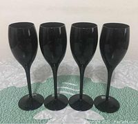 Front view of set of 4 black wine glasses showing tall slender stems and rounded bowls with deep black glossy finish.