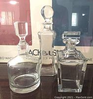 Photo showing the full set of three clear glass decanters against a background poster