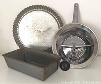 Photo shows all three items: fluted pie pan, loaf pan, and food mill with handle, arranged together.
