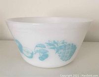 Side view of white milk glass mixing bowl with blue fruit designs including pineapple and cherries.