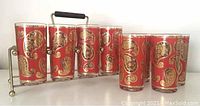 Eight red and gold paisley highball glasses arranged in a metal and wood caddy with handle.