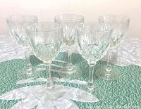 Five vintage crystal liqueur glasses in a row on a tablecloth, showing overall set and shape.