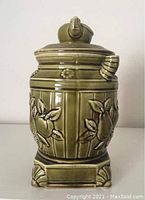 Front side view of green ceramic cookie jar shaped like a vintage pot belly stove with embossed pears and apples and teapot lid.